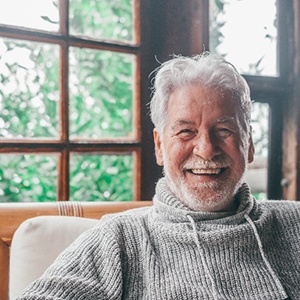 Senior man in gray sweater smiling while relaxing at home