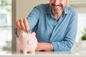 man putting coins into a pink piggy bank 