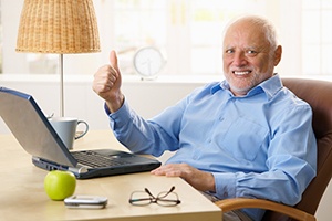 Senior man sitting in front of laptop giving thumbs up