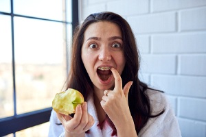A young girl touching her braces and appearing shocked after biting into an apple