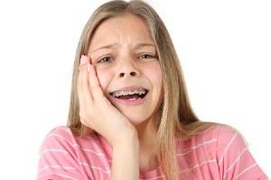 A young girl wearing a pink shirt holds her cheek because of discomfort