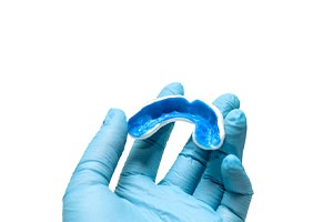 A gloved hand holding a mouthguard for a person who plays sports and wears braces
