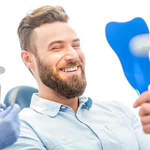 Man in dental chair looking at smile in mirror