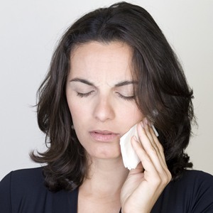 Woman in pain holding cold compress to cheek before occlusal splint treatment