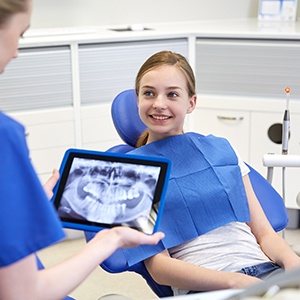 Young girl smiling at dentist holding digital x-rays on tablet computer