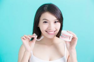 A woman holding a clear tray and a model of braces