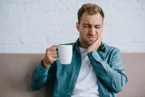 Man on couch with toothache rubbing his jaw