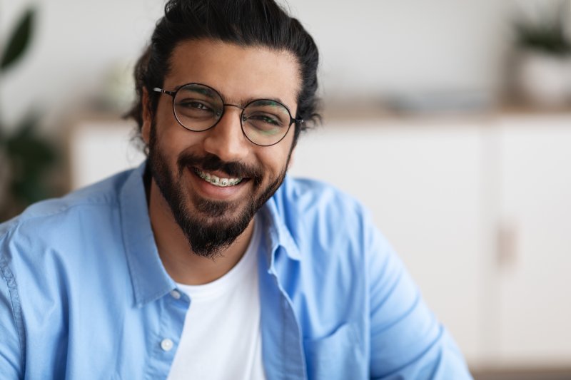 A closeup of an adult man wearing braces and eyeglasses