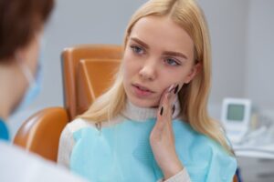 woman holding her face with a dental emergency in the dentist’s chair